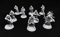 A set of unpainted gray tabletop gaming miniatures depicting soldiers in combat poses, arranged on a black textured background.