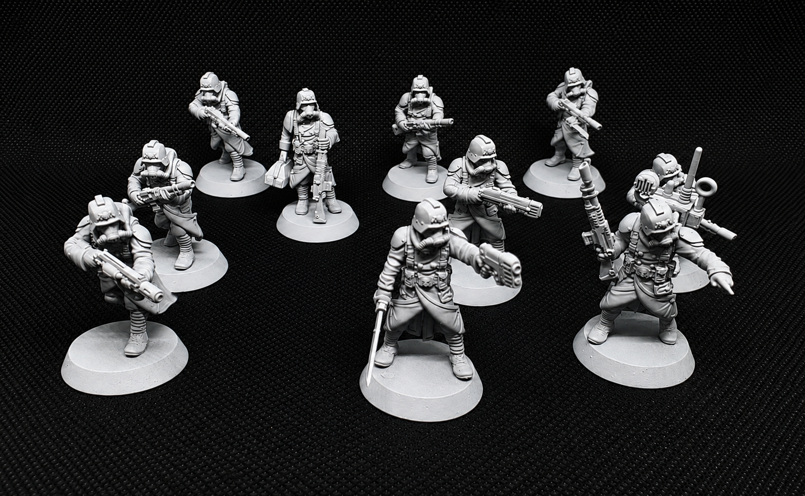 A set of unpainted gray tabletop gaming miniatures depicting soldiers in combat poses, arranged on a black textured background.