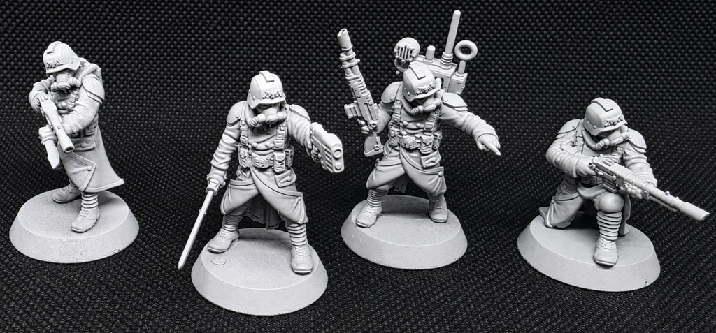 Four unpainted gray tabletop gaming miniatures in different combat poses, displayed on circular bases against a black textured background.