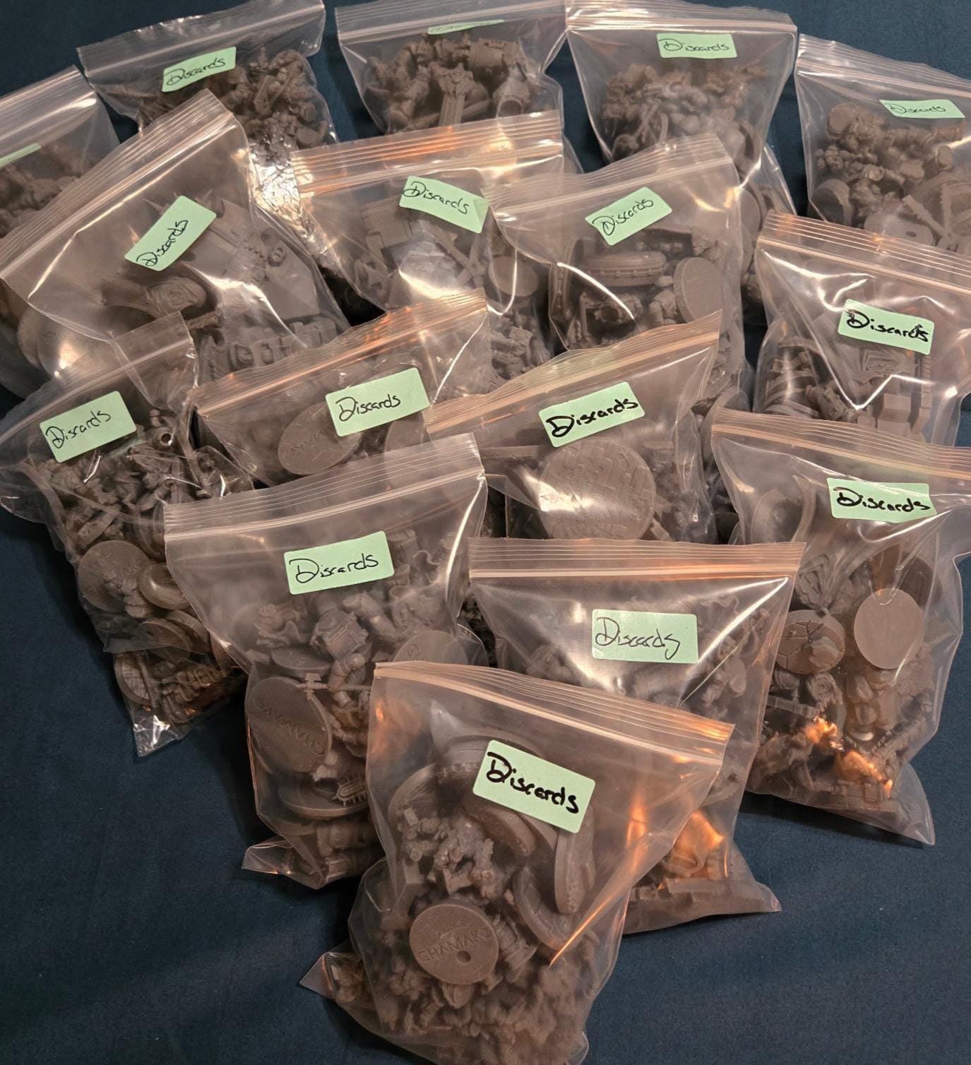 Clear bags filled with assorted resin misprints and discarded miniature parts, including bases, limbs, weapons, armor pieces, and mixed grimdark, sci‑fi, and fantasy bits.