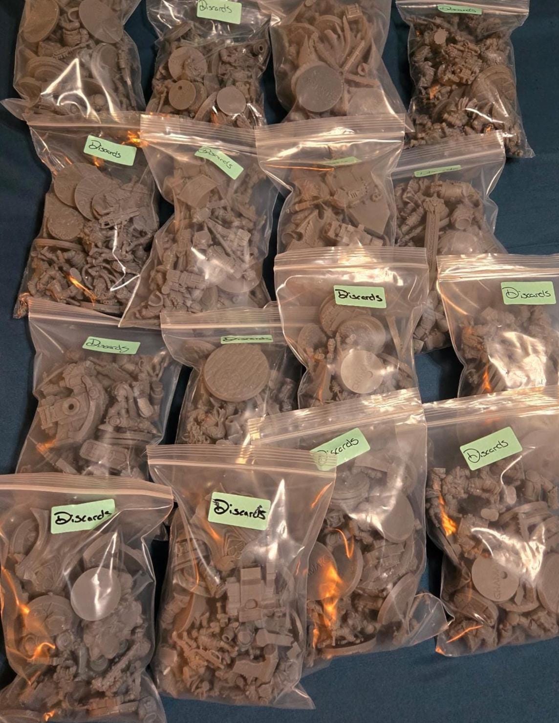 Clear bags filled with assorted resin misprints and discarded miniature parts, including bases, limbs, weapons, armor pieces, and mixed grimdark, sci‑fi, and fantasy bits.